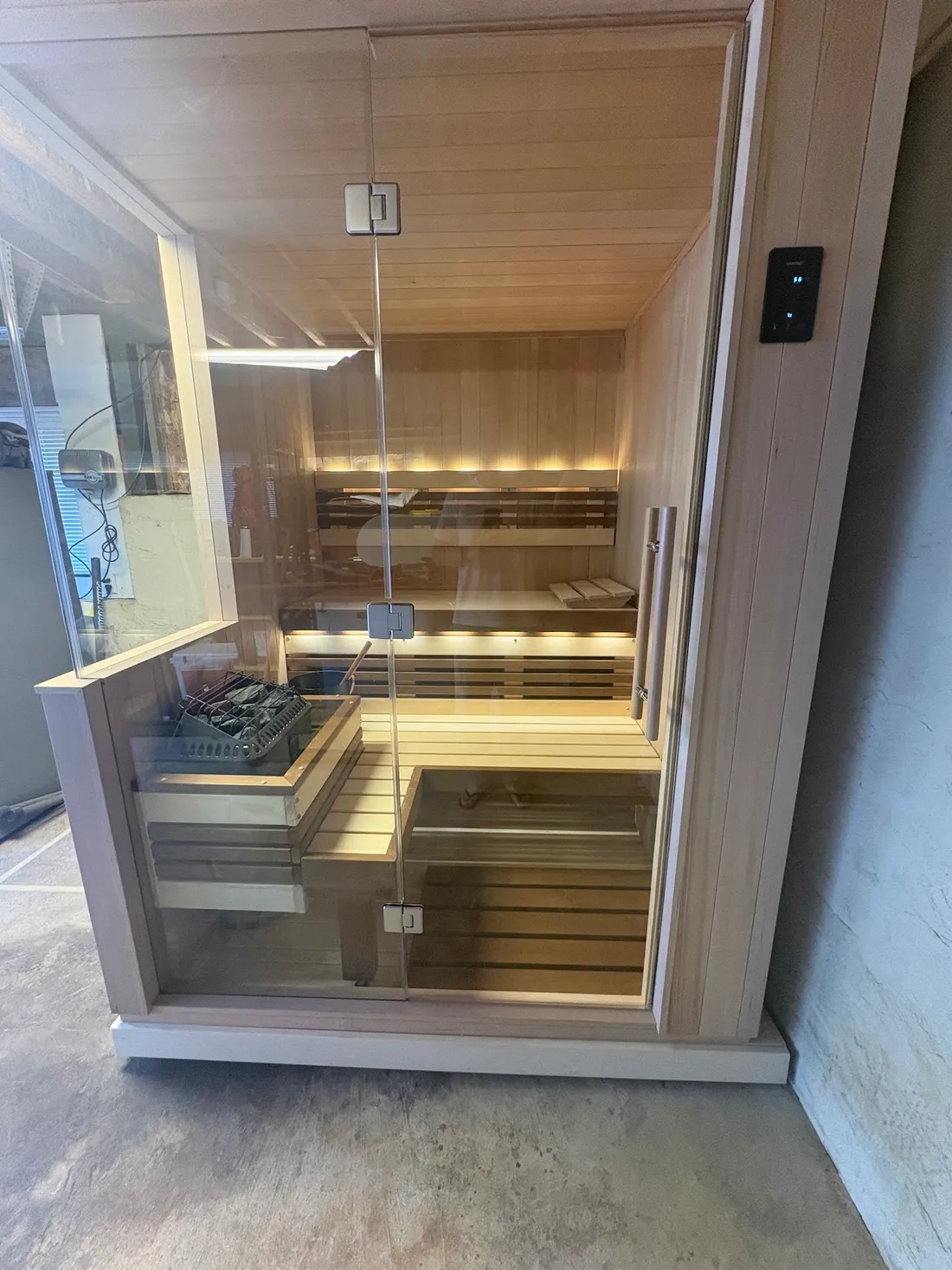 A glass-walled indoor sauna with lit benches and the heater beside them, Mill Valley
