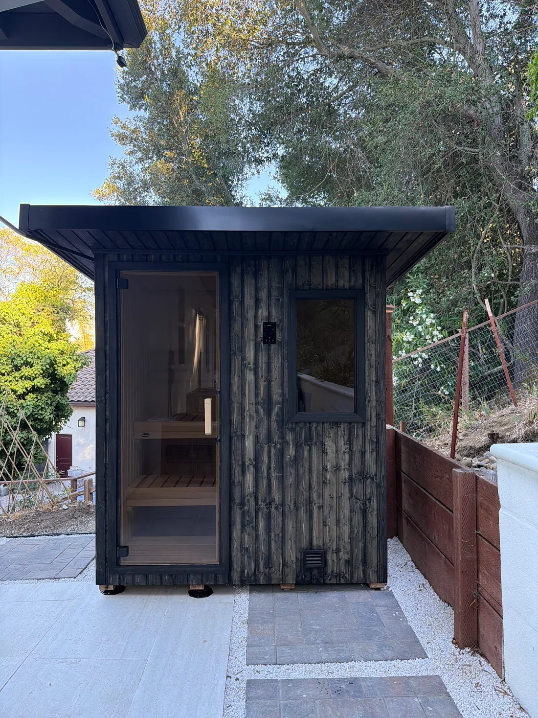 A dark outdoor sauna cabin with a glass door and a window, Pleasanton