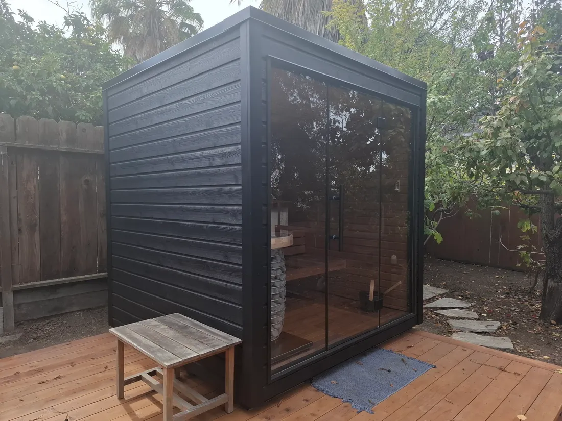 A black-clad outdoor cabin sauna with a glass front on a backyard deck, Oakland