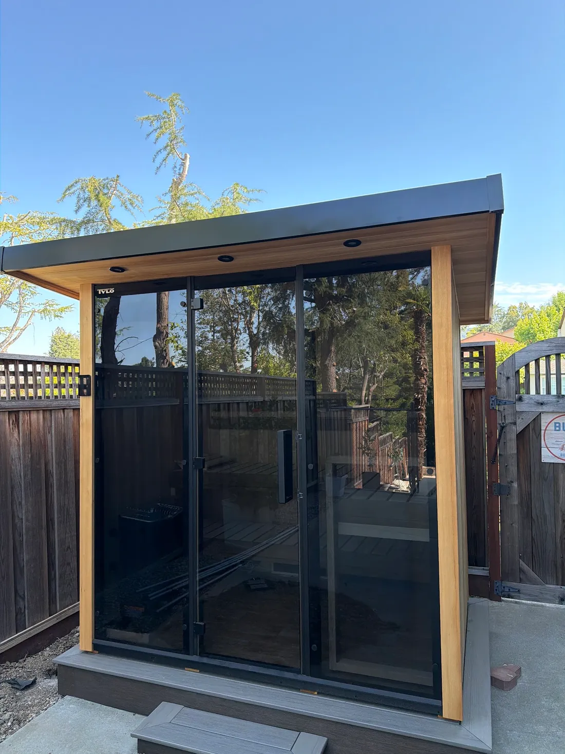 An outdoor sauna with a glass front and a flat roof in a backyard, San Jose