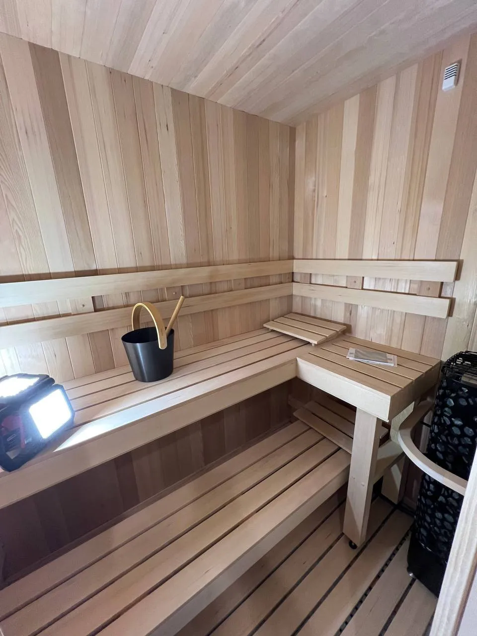 Cedar interior with an L-shaped upper bench, a bucket and the heater beside it