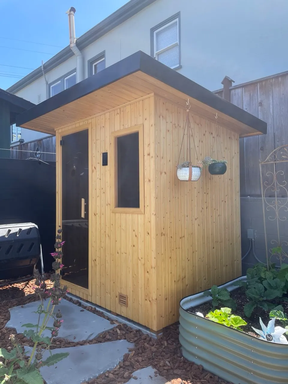 A compact outdoor sauna with a glass door in a backyard