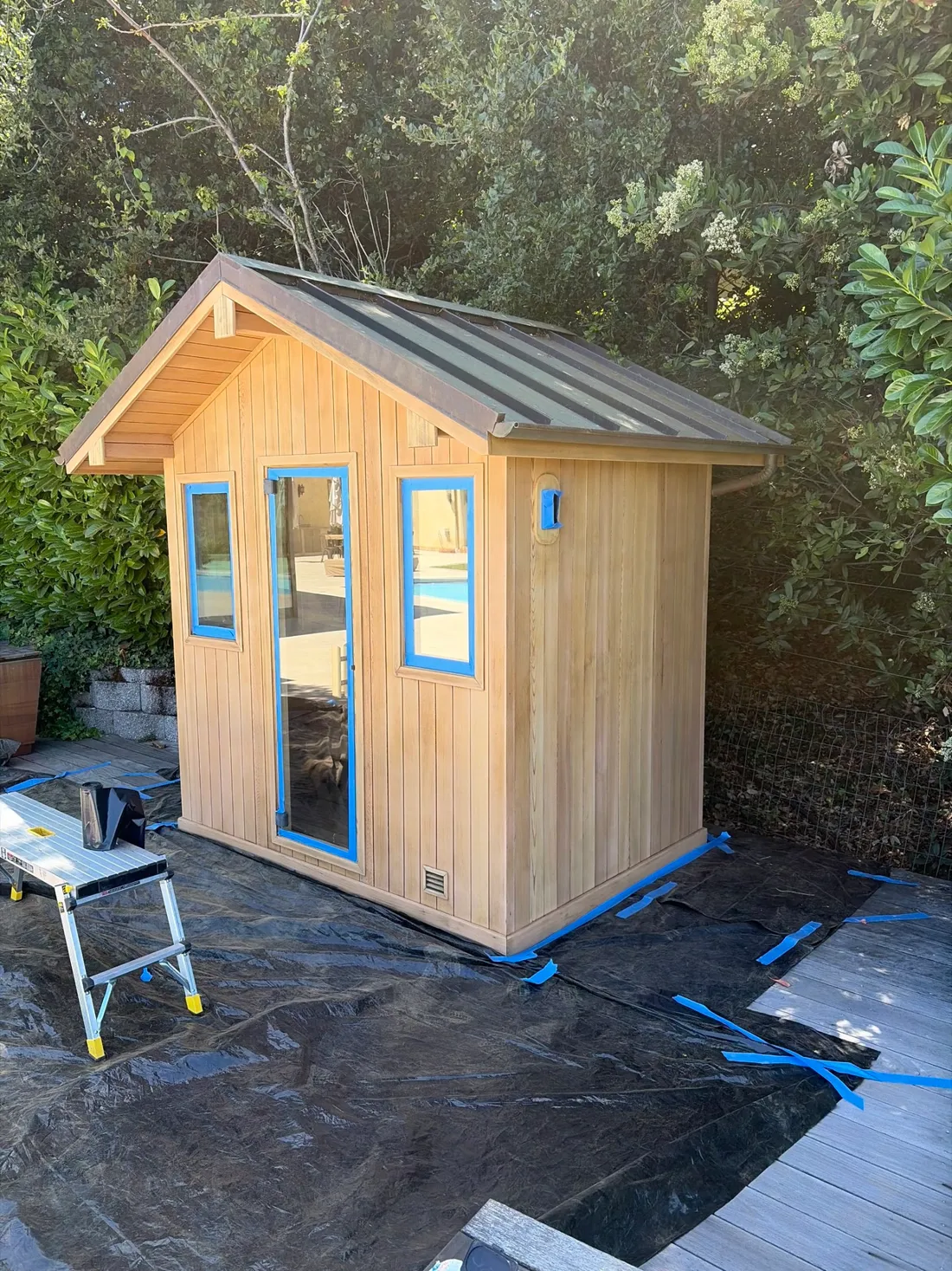 A gabled outdoor sauna cabin with a glass door and windows
