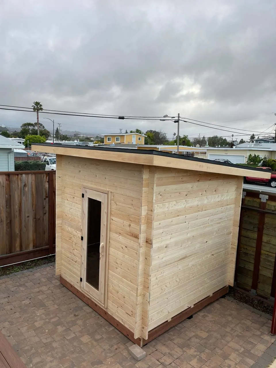 A flat-roofed outdoor sauna cabin on a paved yard